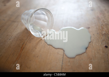 Bicchiere di latte rovesciato sul pavimento in legno Foto Stock