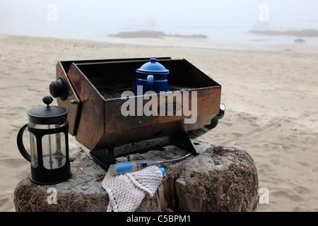 Rendendo l'acqua calda per il tè e il caffè camping su di una spiaggia di sabbia in una nebbiosa mattina di luglio Foto Stock
