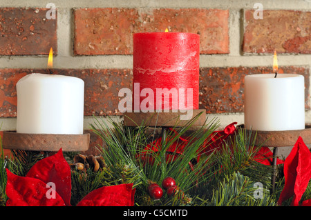 Tre candele di Natale su sempreverdi e poinsettia con un sfondo mattone Foto Stock