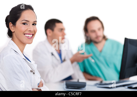 Sorridente giovane medico con altri medici dietro di lei su sfondo bianco Foto Stock