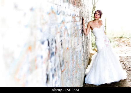 Sposa pone contro il muro di graffiti in abito da sposa guardando lontano Foto Stock