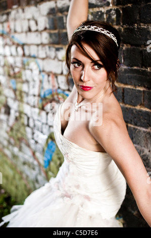 Sposa pone contro il muro di graffiti in abito da sposa guardando lontano Foto Stock