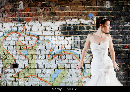 Sposa pone contro il muro di graffiti in abito da sposa guardando lontano Foto Stock
