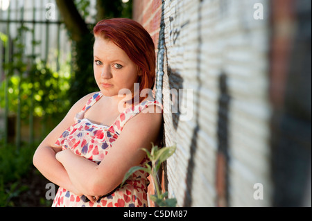 Un moody cercando dai capelli rossi 15 16 enne ragazza adolescente. con le braccia piegate appoggiato contro una parete REGNO UNITO Foto Stock