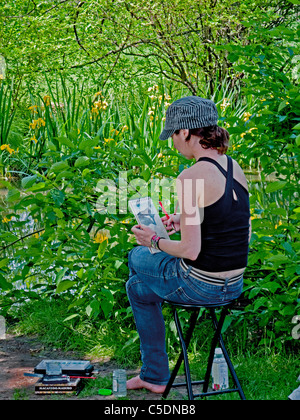 Una giovane donna artista lavora su un disegno mentre è seduto in un boschetto di iris al Brooklyn Botanic Garden in New York City. Foto Stock