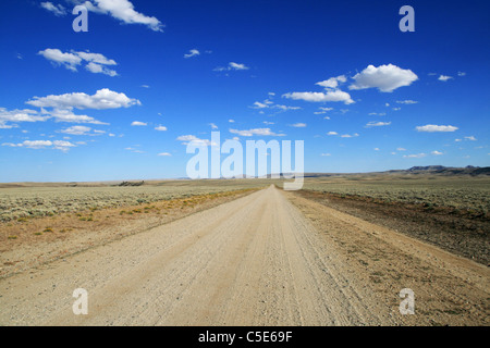 Lonely strada sterrata che corre attraverso le pianure del Wyoming a un lontano orizzonte con il cielo blu e nuvole Foto Stock