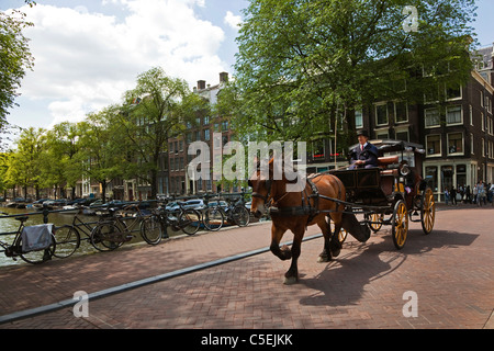 Turisti in un cavallo e carrozza di essere prese in considerazione per un giro intorno al centro della cittã di Amsterdam, attraverso un ponte e su un canale Foto Stock