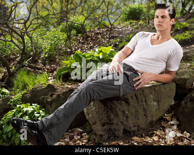 Foto di un elegante giovane uomo seduto su una roccia in un giardino Foto Stock