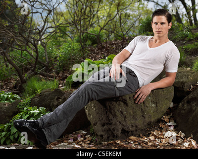 Foto di un elegante giovane uomo seduto su una roccia in un giardino Foto Stock