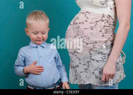 Funny little boy toccando il suo ventre accanto a sua madre in stato di gravidanza Foto Stock