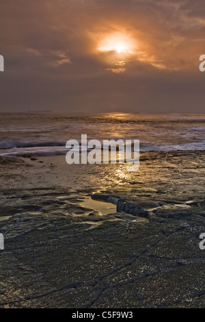 Sunbursting attraverso le nuvole all'alba, guardando fuori attraverso il mare dalla spiaggia di Bamburgh, Northumberland Foto Stock