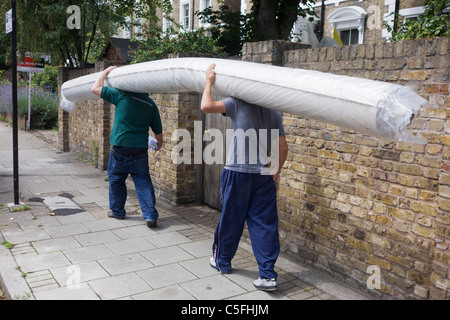 Due operai di consegna il trasporto di un rotolo pesante del tappeto lungo la South London street. Foto Stock