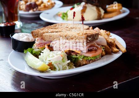 Tacchino affumicato, prosciutto affumicato, pancetta affumicata, il formaggio svizzero e formaggio cheddar, lattuga, pomodoro, cipolla, mayo servita su fette di pane tostato Foto Stock