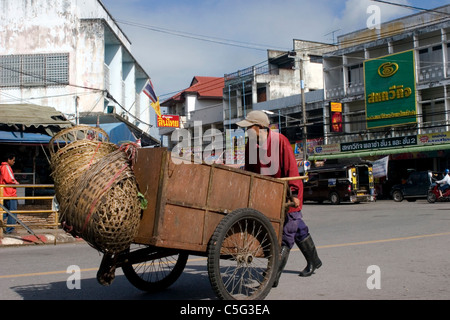 Un uomo sta spingendo un carrello di legno con cesti legato sulla parte anteriore su una strada di città nel nord della Thailandia. Foto Stock