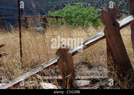 Le stecche di un Picket Fence cadono verso il basso dietro il più moderno Filo spinato in quella parzialmente abbandonato città di Cuervo, Nuovo Messico. Foto Stock