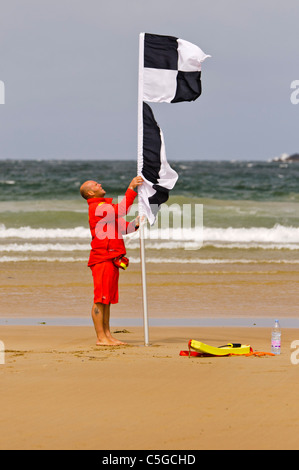 Bagnino RNLI erige in bianco e nero a scacchi in surfers bandiera nuotatori di avvertimento che i surfisti e kayak sono nella zona Foto Stock