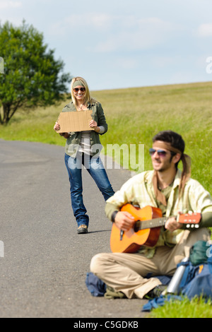 Sollevatore-escursione coppia giovane zaino tramping su strada asfaltata suonare la chitarra Foto Stock