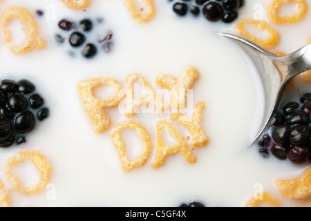 Le parole il giorno di paga enunciato alla lettera a forma di pezzi di cereali galleggianti in un latte riempito ciotola di cereale. Foto Stock