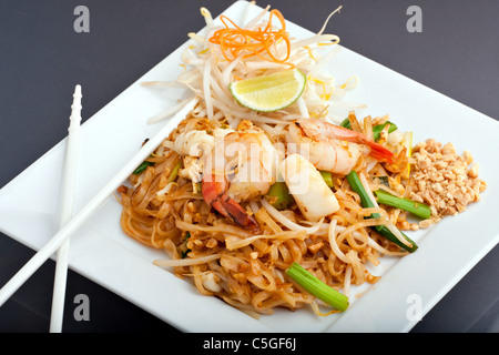 Tampone di pesce piatto tailandese di Thai fried rice noodles su un quadrato bianco con piastra di bacchette e carote grattugiate guarnire. Foto Stock