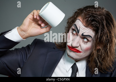 Ritratto di imprenditore con faccia dipinta guardando a tazza da caffè Foto Stock