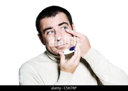 Ritratto di un uomo caucasico inserendo una lente a contatto nel Suo occhio in studio isolato su bianco sfondo isolato Foto Stock