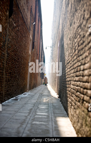 Una donna cammina in una strada stretta che porta le borse della spesa, Venezia, Italia Foto Stock