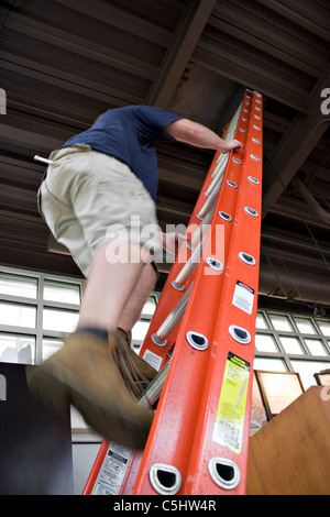 Un uomo che lavora un lavoro HVAC sale una scala fino al tetto apribile. Foto Stock