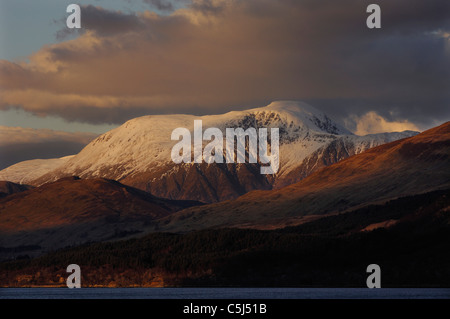 Il cuore illuminato, coperta di neve vertice del Ben Nevis, Scozia montagna più alta, sorge sopra dark pedemontana, visto da di Ardgour, Foto Stock