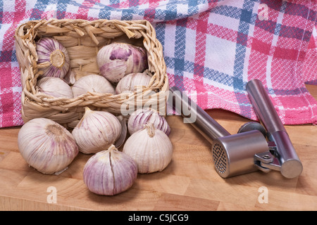 Ein Körbchen mit Knoblauchknollen, eine Knoblauchpresse liegt daneben | un piccolo cestino di aglio, una pressa aglio è a fianco Foto Stock