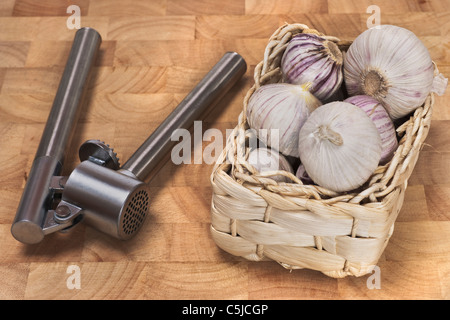 Ein Körbchen mit Knoblauchknollen, eine Knoblauchpresse liegt daneben | un piccolo cestino di aglio, una pressa aglio è a fianco Foto Stock