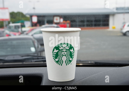 Starbucks monouso di caffè da asporto per andare in un asporto bicchiere di carta per andare con il nuovo logo su un cruscotto di automobile in una stazione di servizio autostradale. Inghilterra, Regno Unito Foto Stock