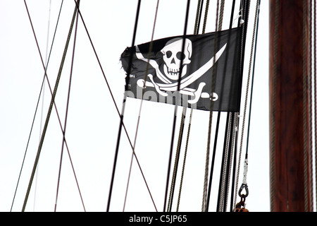 Un ragged bianco e nero bandiera pirata nel montante di una barca a vela di prendere un sacco di vento , immagine concettuale , metafora Foto Stock