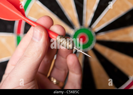 Una mano che tiene un dardo ottenere pronto a mirare il dartboard. Profondità di campo. Foto Stock
