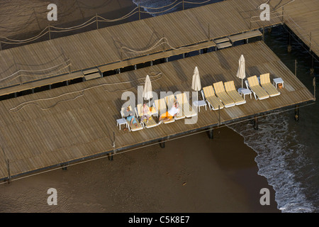 Vista aerea di tre persone giacenti su sedie reclinabili sul molo in legno, Lara, Antalya, Turchia Foto Stock