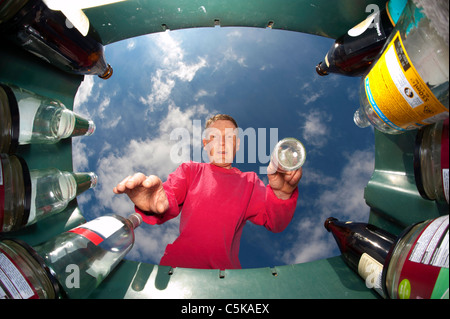 Uomo di gettare una bottiglia di vetro nel verde del contenitore di riciclaggio per il riciclaggio Foto Stock