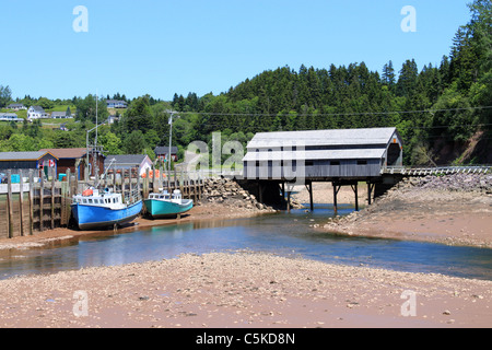 La pesca wharf a Saint Martins, New Brunswick, Canada sulla bassa marea con barche ormeggiate nel fango con un ponte coperto in background Foto Stock