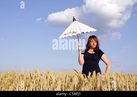 Giovane donna in piedi con poco bianco ombrello nel campo di frumento. Foto Stock