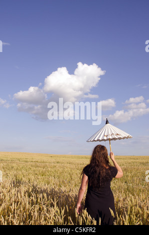 Retro della giovane donna a piedi con poco bianco ombrello nel campo di frumento. Foto Stock