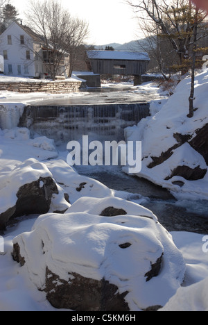 Con un ponte coperto in background, l'acqua scorre su una diga in inverno a Warren, Vermont. Foto Stock