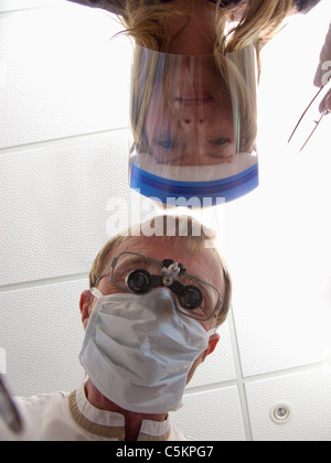 Un dentista con maschera e lente di ingrandimento binoculari ed un infermiere indossare occhiali o una visiera parasole, visto da un paziente, eyeview Wellington, Nuova Foto Stock