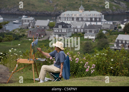 Monhegan Island, Maine -- donna artista dipinge utilizzando un easle sulla cima di una collina che si affaccia Monhegan Island Harbour e villaggio, Foto Stock