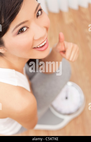 Sopra la testa vista di felice & bella asiatica orientale donna cinese del peso di se stessa su scale in palestra o club salute Foto Stock