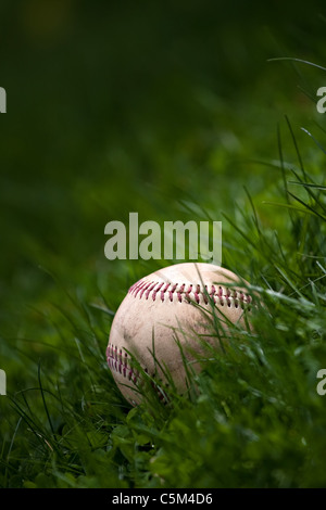 Uno invecchiato e indossato il baseball in seduta l'erba verde. Foto Stock