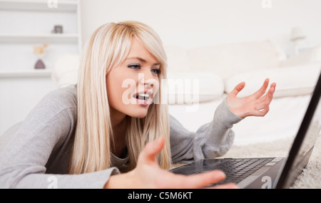 Bella donna bionda frustrati con il suo computer giacente su un tappeto Foto Stock