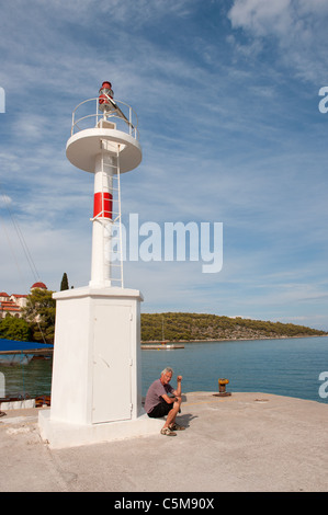 Uomo seduto vicino al faro di luce nel porto greco Nea Epidavros Foto Stock