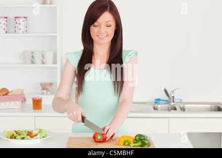 Interessanti i capelli rossi donna il taglio di alcune verdure in cucina Foto Stock