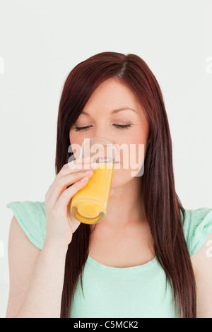 Interessanti i capelli rossi donna bere un bicchiere di succo di arancia in cucina Foto Stock