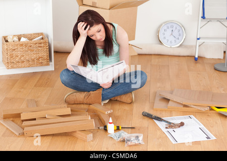 Guardando bene i capelli rossi ragazza essendo premuto durante la lettura di un manuale prima di fai-da-te Foto Stock