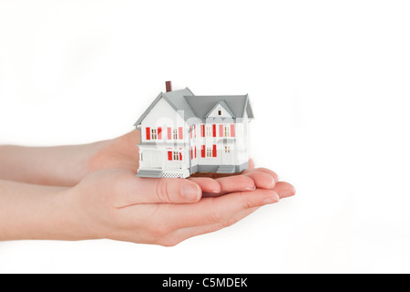 Mani tenendo una casa in miniatura su sfondo bianco Foto Stock