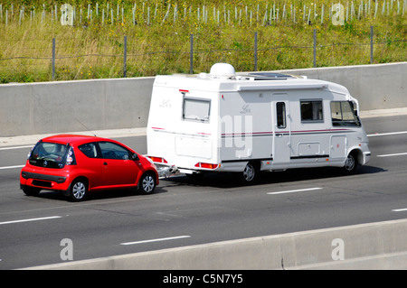 Laterale e posteriore del bianco francese Le Voyageur LVX camper rosso di traino Citreon C1 auto percorrendo l autostrada del Regno Unito per un stile di vita in viaggio Foto Stock
